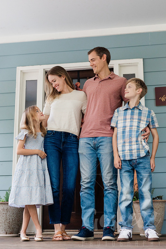 Family of four sitting on their front porch steps, smiling and holding hands in golden afternoon light.