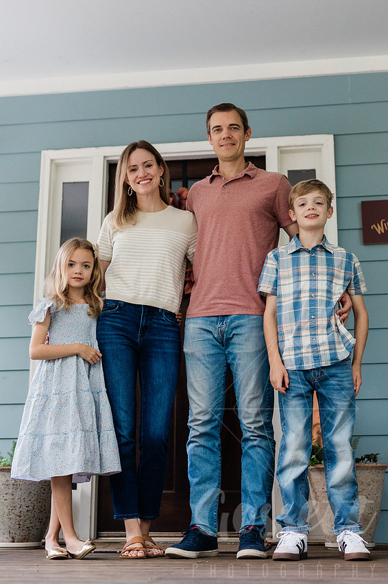Family of four sitting on their front porch steps, smiling and holding hands in golden afternoon light.