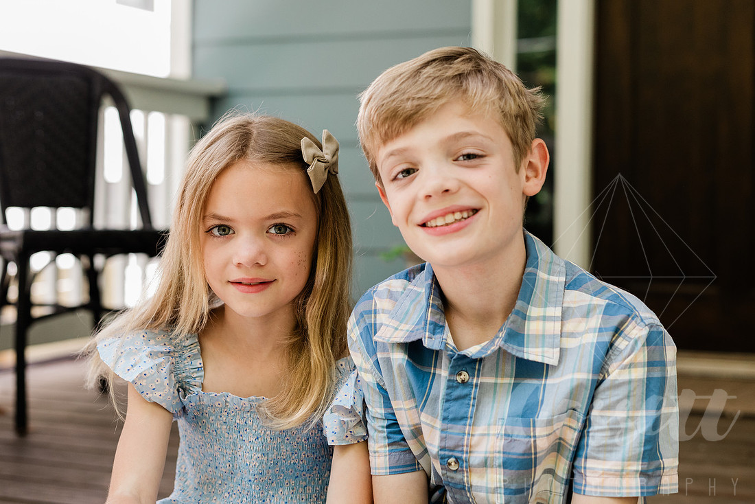 Family of four sitting on their front porch steps, smiling and holding hands in golden afternoon light.