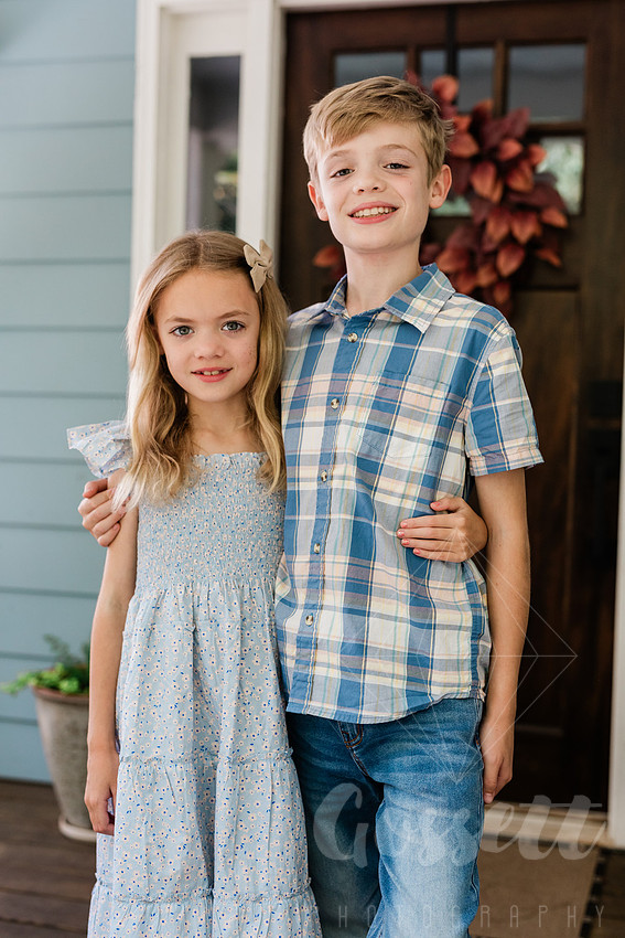 Family of four sitting on their front porch steps, smiling and holding hands in golden afternoon light.