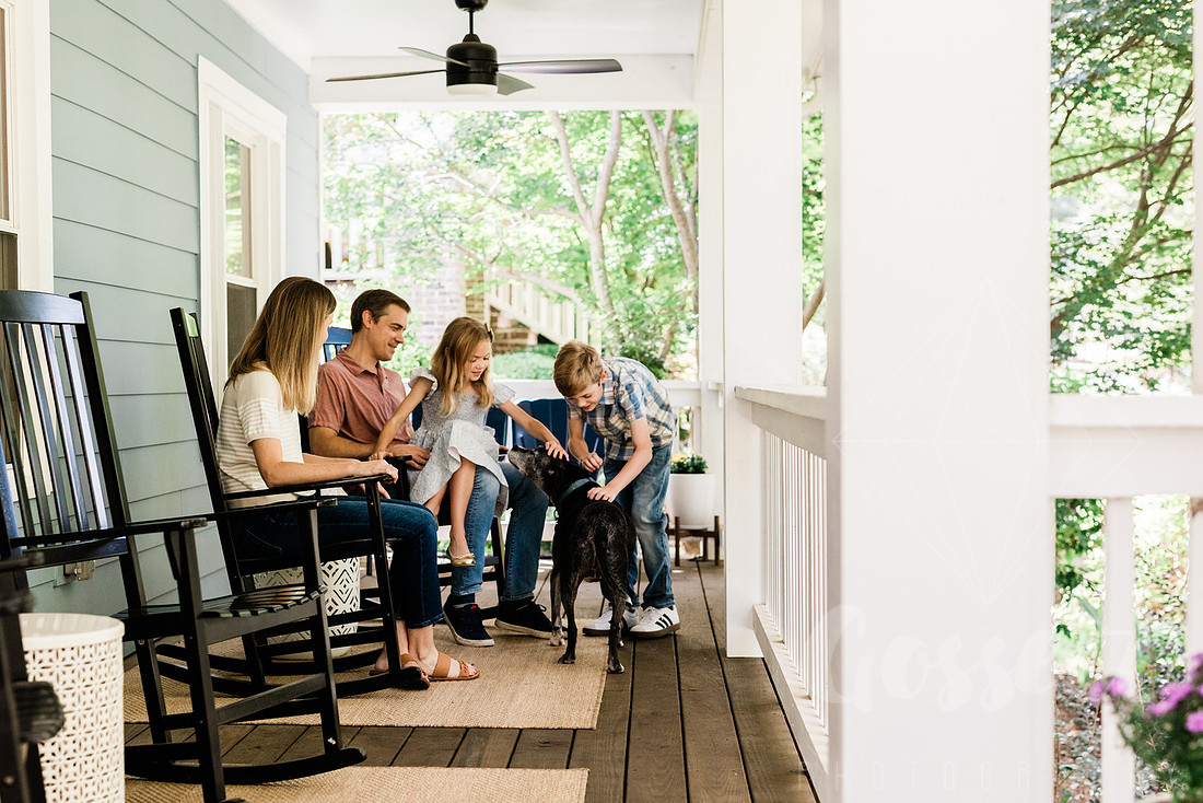 Family of four sitting on their front porch steps, smiling and holding hands in golden afternoon light.