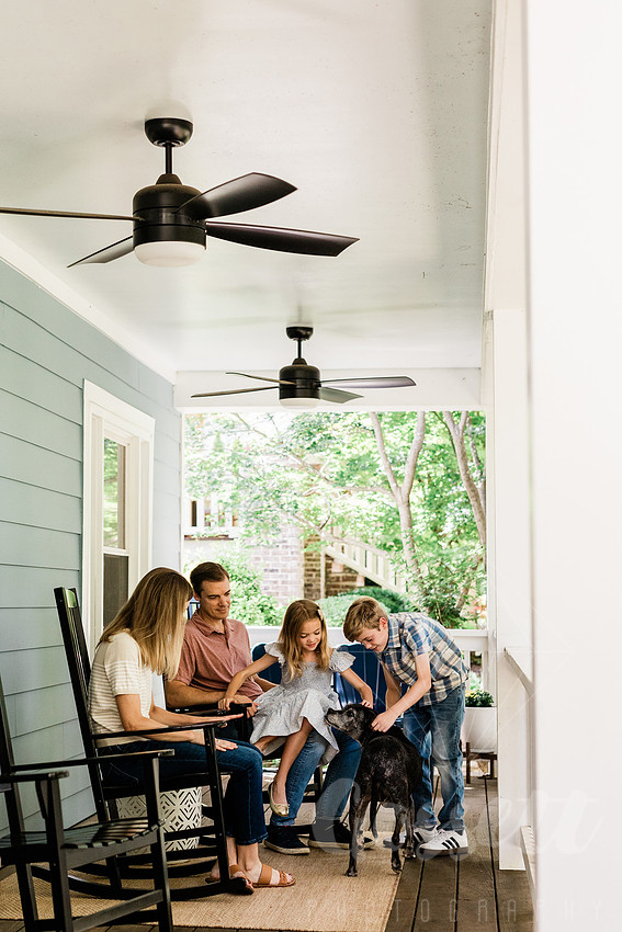 Family of four sitting on their front porch steps, smiling and holding hands in golden afternoon light.