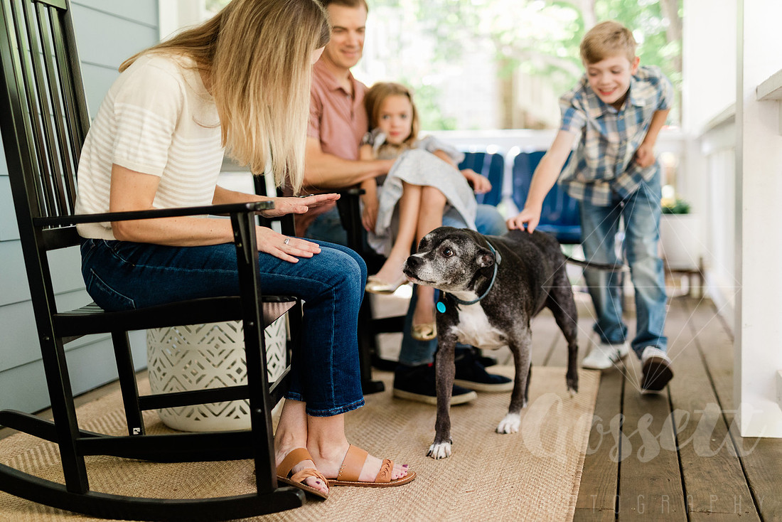 Family of four sitting on their front porch steps, smiling and holding hands in golden afternoon light.