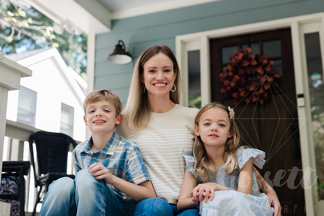 Family of four sitting on their front porch steps, smiling and holding hands in golden afternoon light.