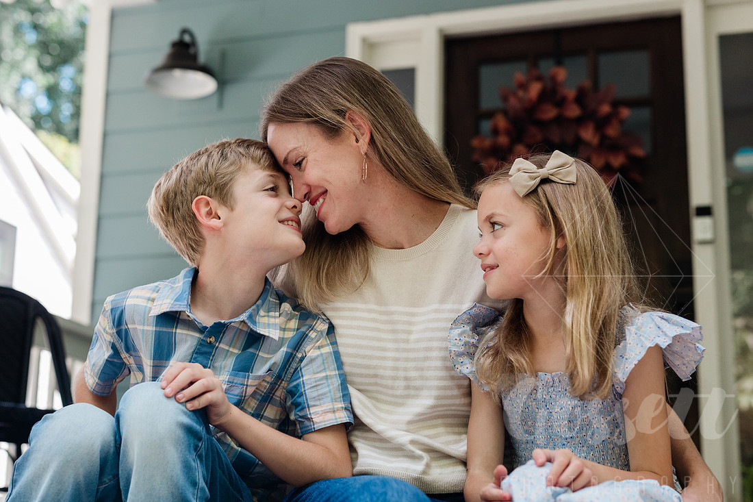 Family of four sitting on their front porch steps, smiling and holding hands in golden afternoon light.