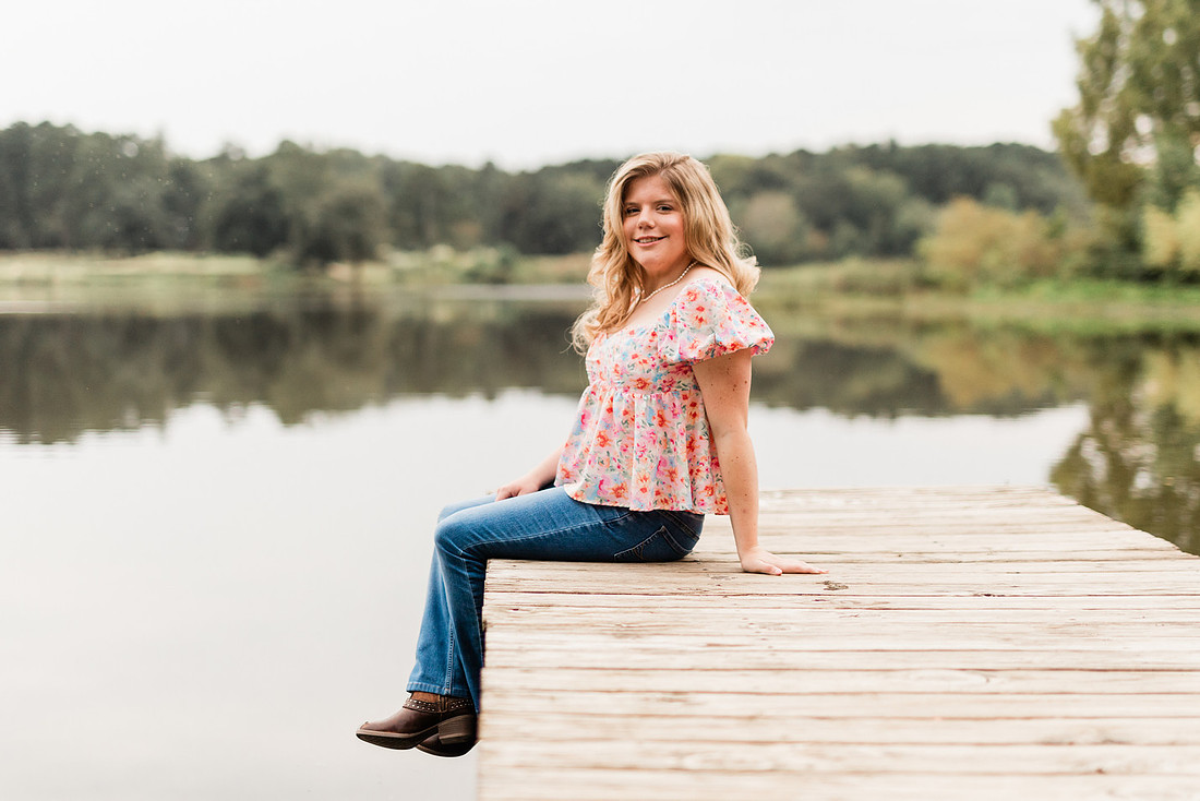 Senior in high school poses for senior session on a dock. 