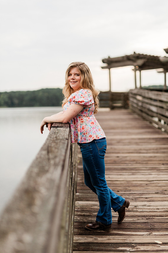 Senior in high school poses for senior session on a dock. 