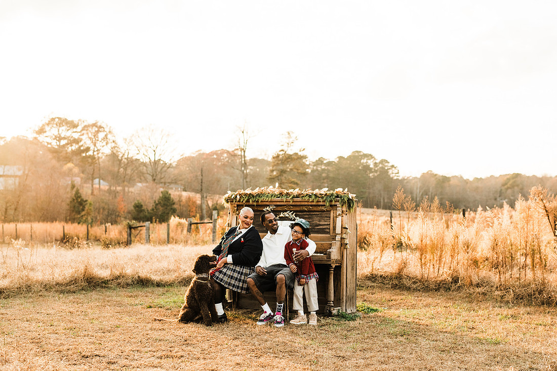 Family gathered around a vintage piano in a golden field for a holiday session. 