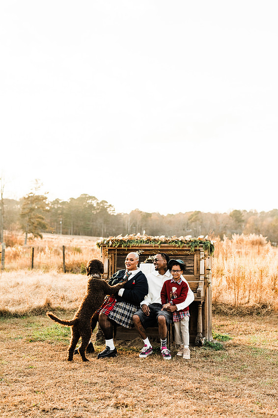 Family gathered around a vintage piano in a golden field for a holiday session. 