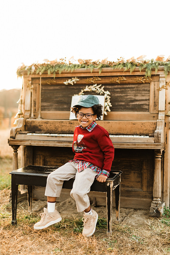 Family gathered around a vintage piano in a golden field for a holiday session. 