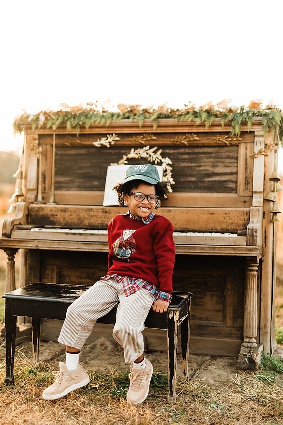 Family gathered around a vintage piano in a golden field for a holiday session. 