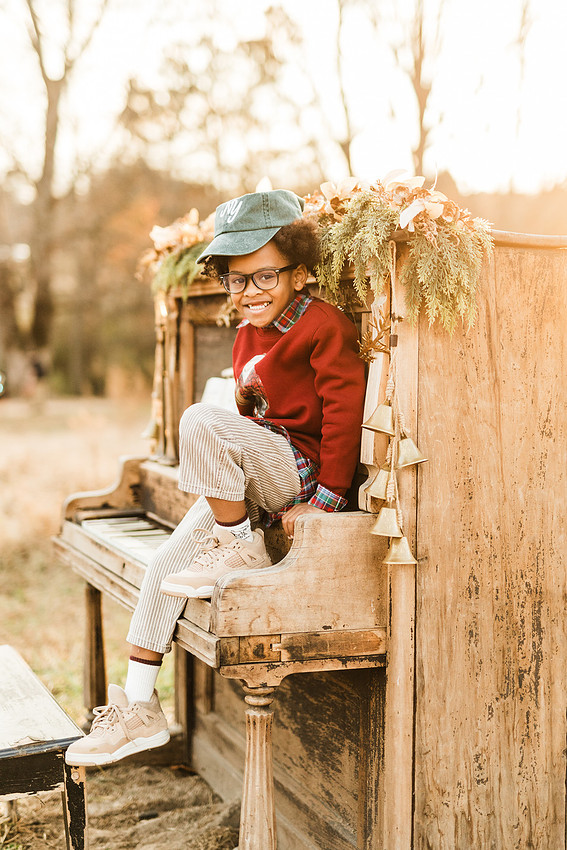 Family gathered around a vintage piano in a golden field for a holiday session. 