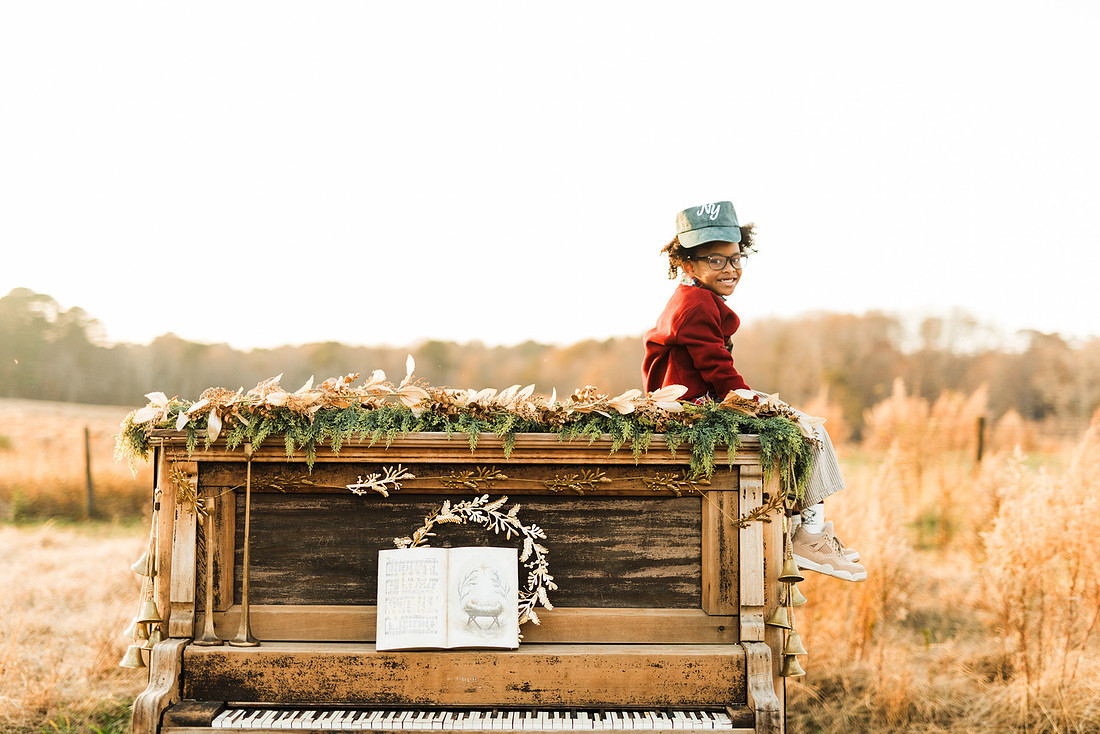Family gathered around a vintage piano in a golden field for a holiday session. 