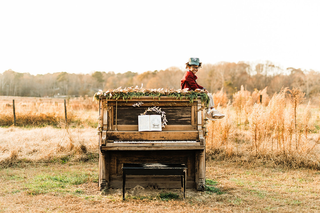 Family gathered around a vintage piano in a golden field for a holiday session. 