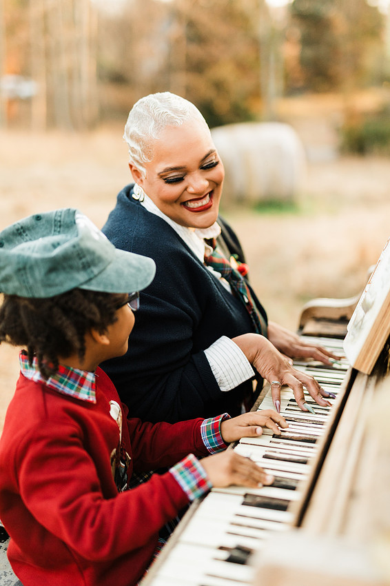 Family gathered around a vintage piano in a golden field for a holiday session. 