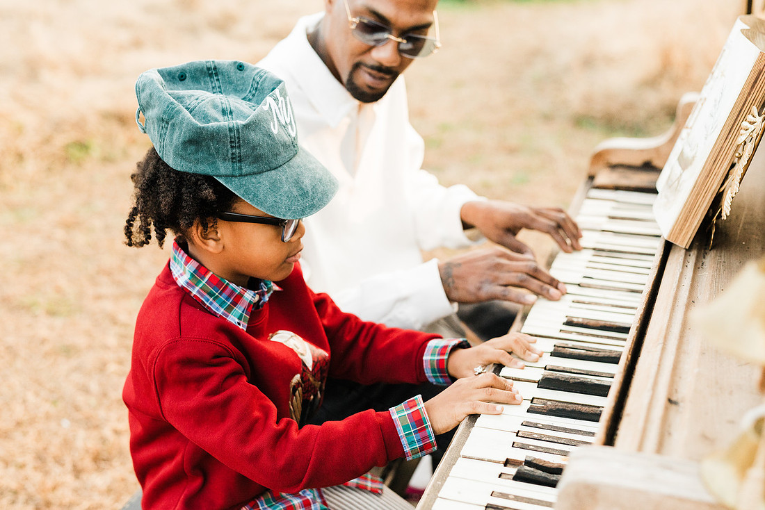 Family gathered around a vintage piano in a golden field for a holiday session. 