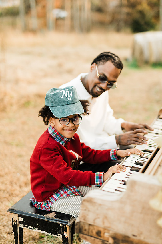 Family gathered around a vintage piano in a golden field for a holiday session. 