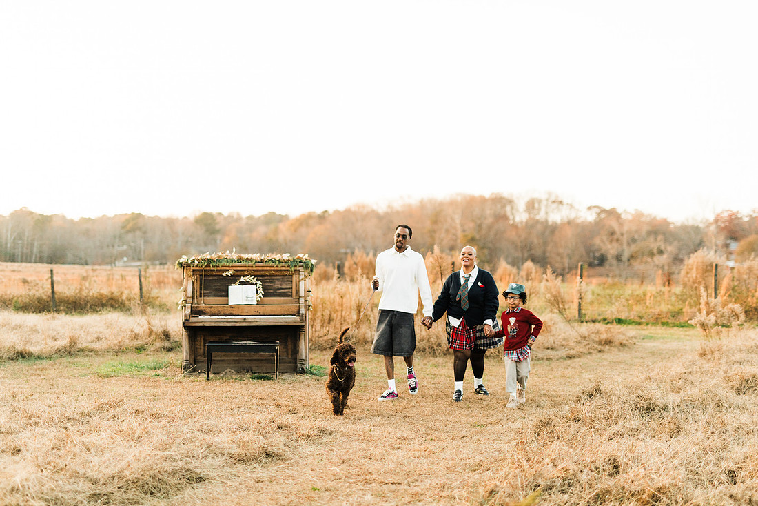 Family gathered around a vintage piano in a golden field for a holiday session. 