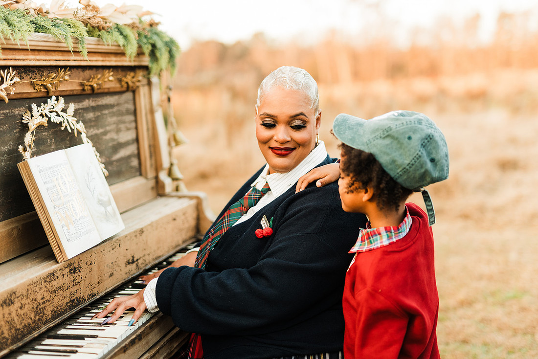 Family gathered around a vintage piano in a golden field for a holiday session. 