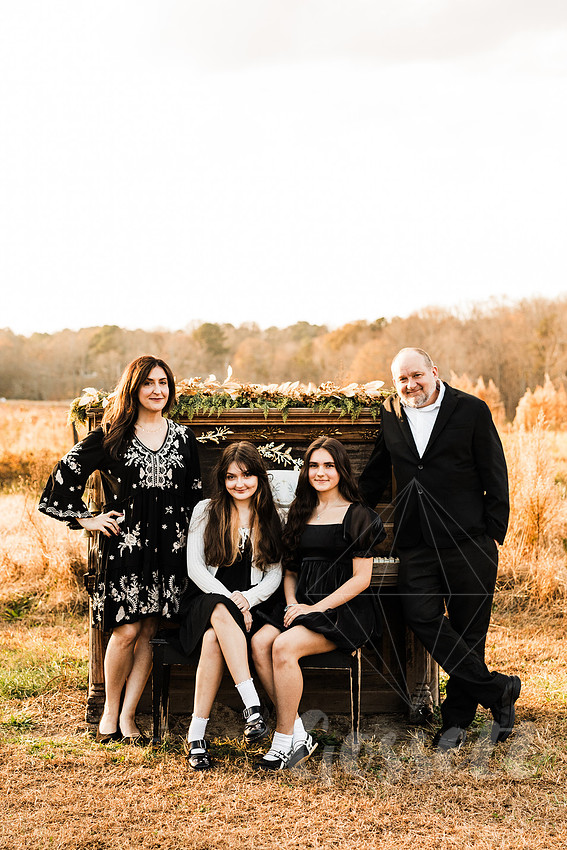 a family gathers around a vintage piano in a golden field for a christmas mini session