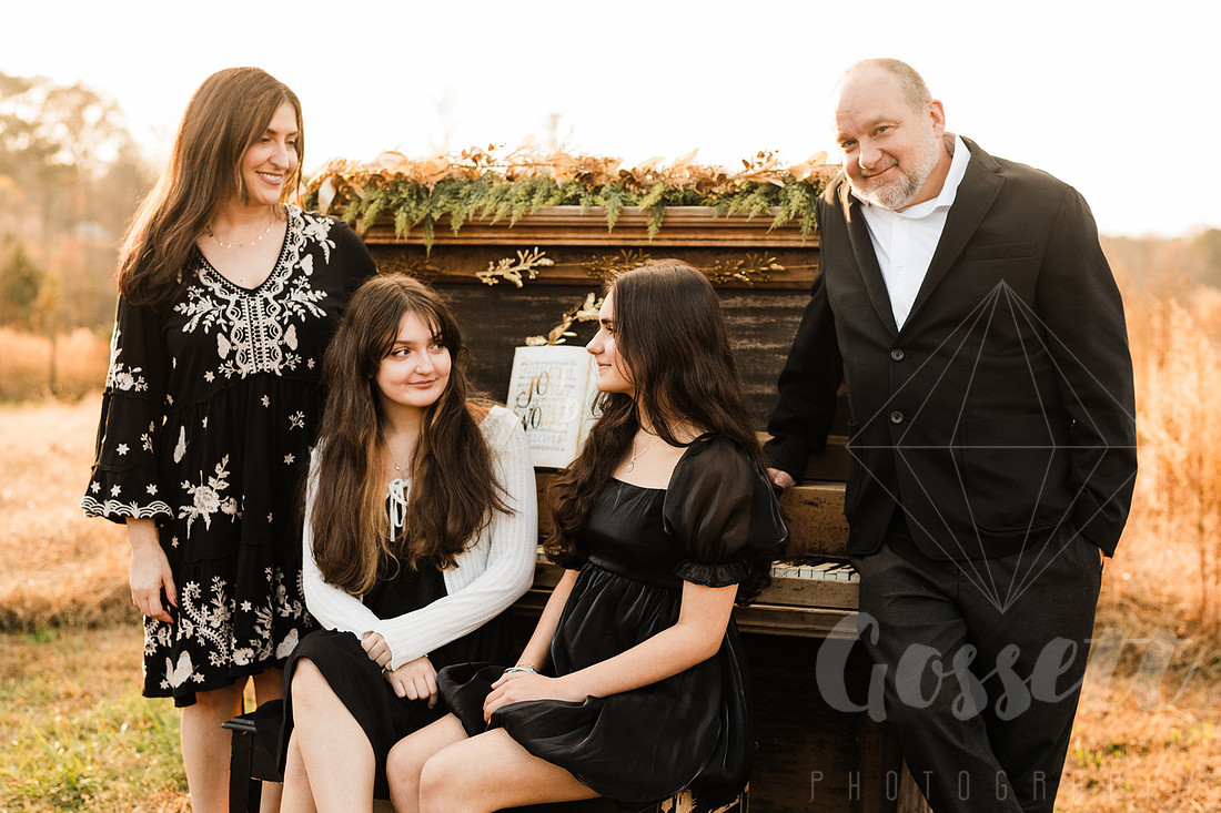a family gathers around a vintage piano in a golden field for a christmas mini session