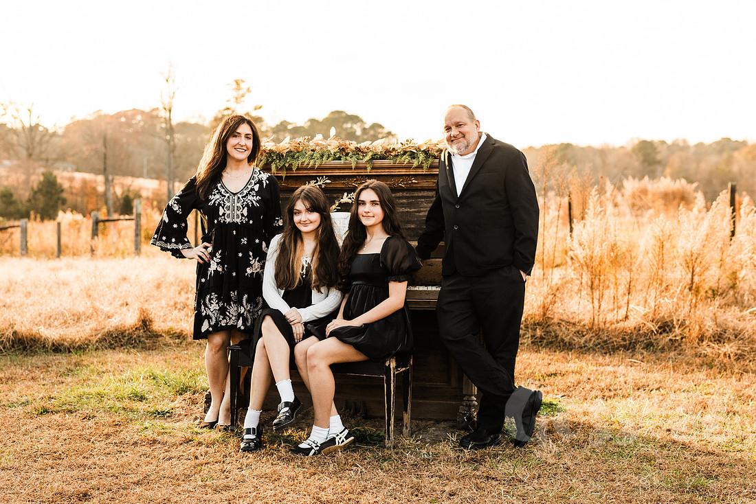 a family gathers around a vintage piano in a golden field for a christmas mini session