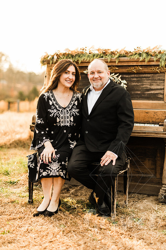a family gathers around a vintage piano in a golden field for a christmas mini session