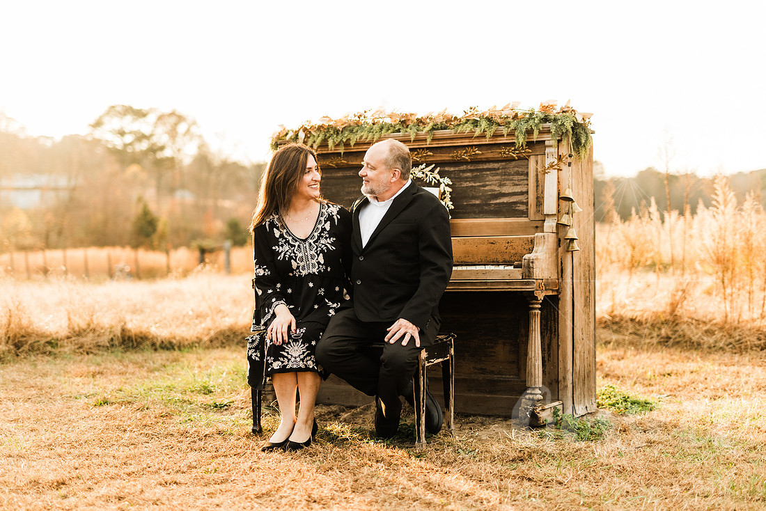 a family gathers around a vintage piano in a golden field for a christmas mini session