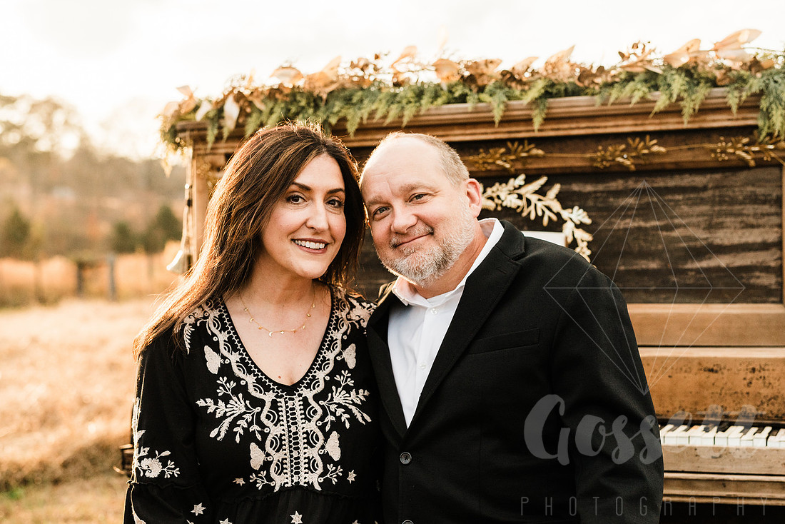 a family gathers around a vintage piano in a golden field for a christmas mini session