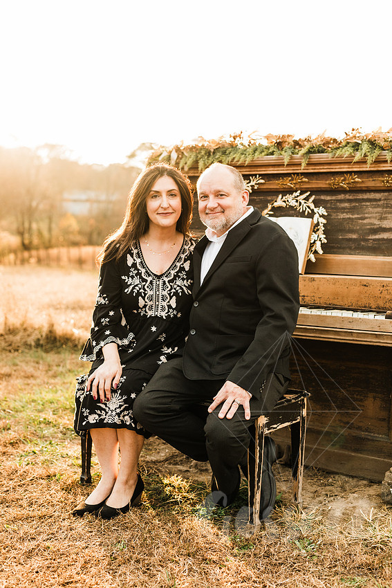 a family gathers around a vintage piano in a golden field for a christmas mini session