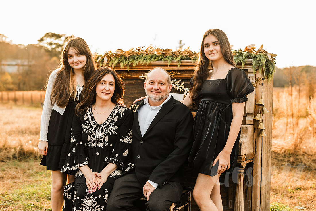 a family gathers around a vintage piano in a golden field for a christmas mini session