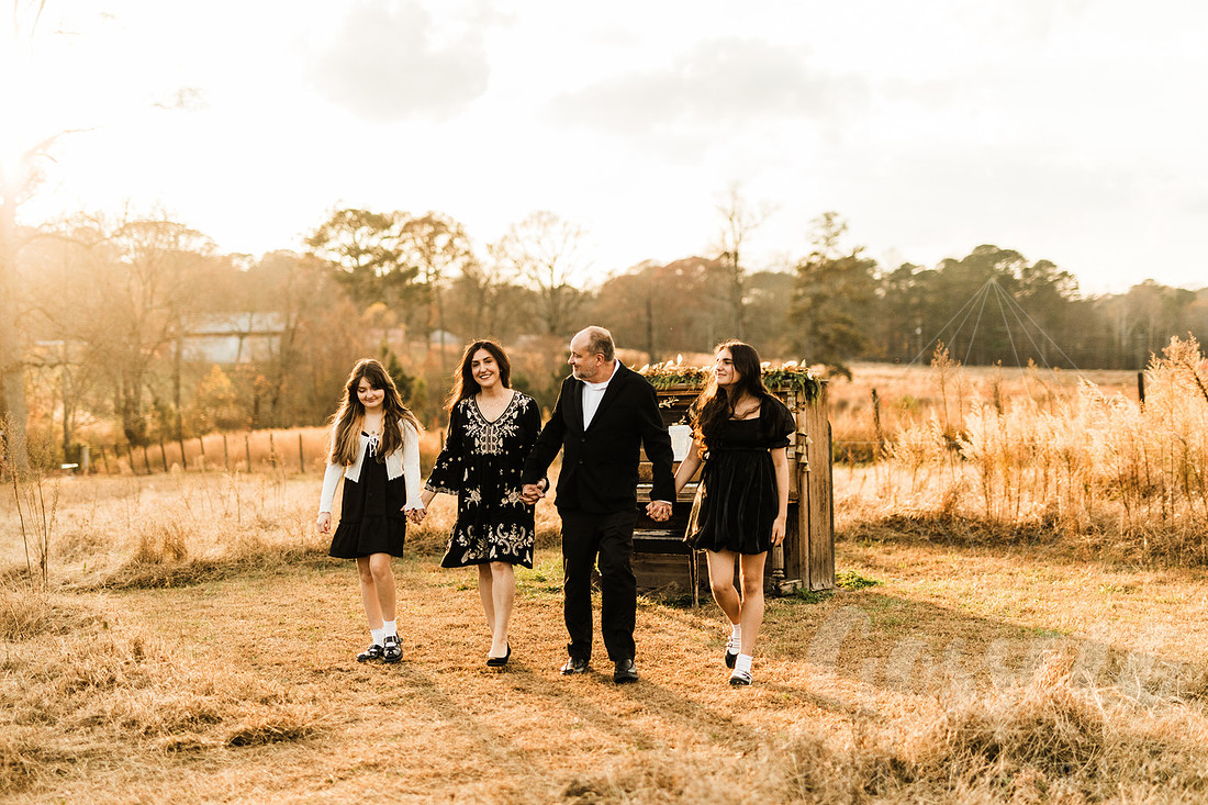 a family gathers around a vintage piano in a golden field for a christmas mini session