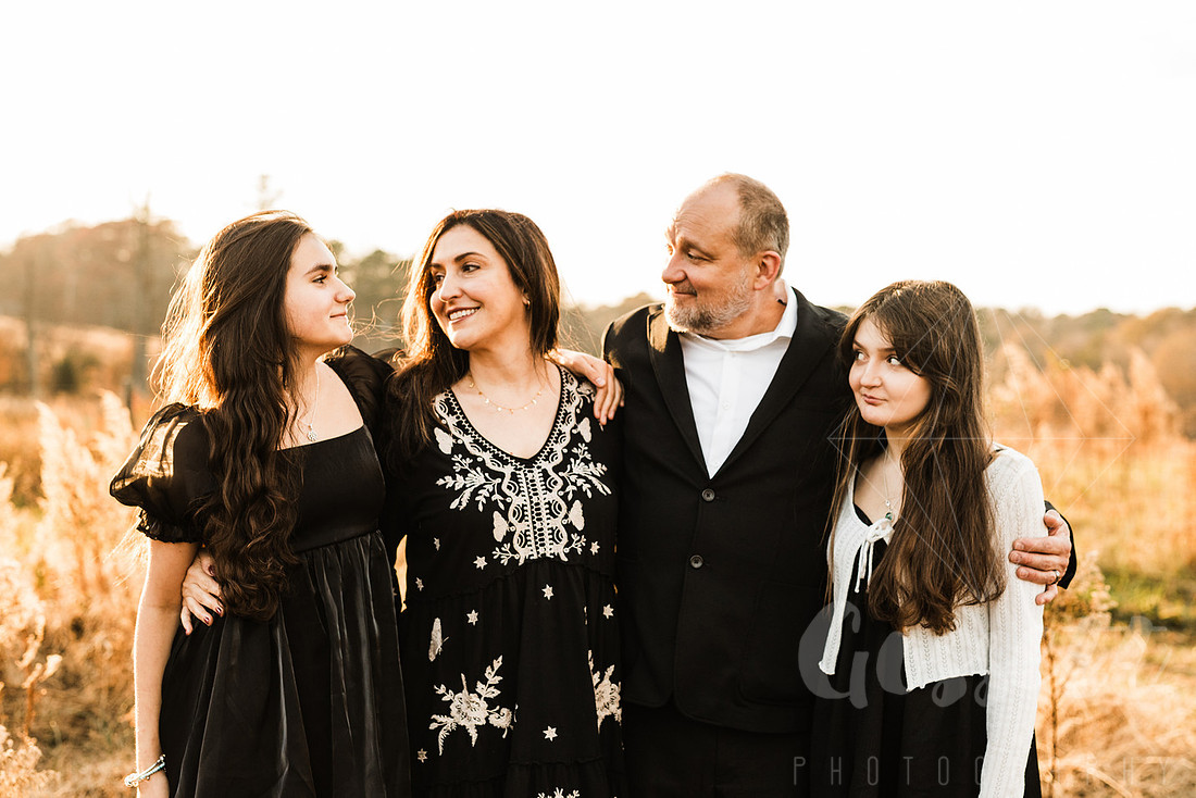 a family gathers around a vintage piano in a golden field for a christmas mini session