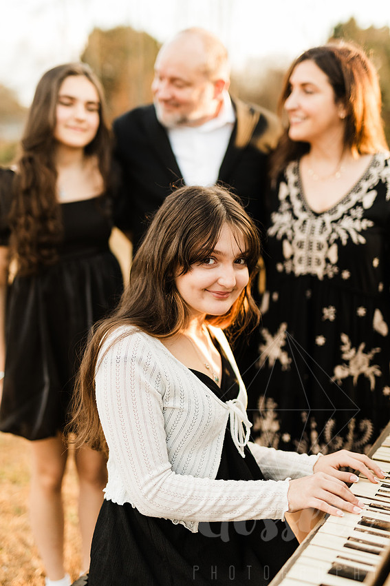 a family gathers around a vintage piano in a golden field for a christmas mini session
