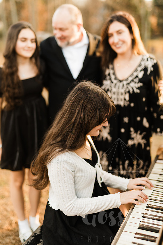 a family gathers around a vintage piano in a golden field for a christmas mini session
