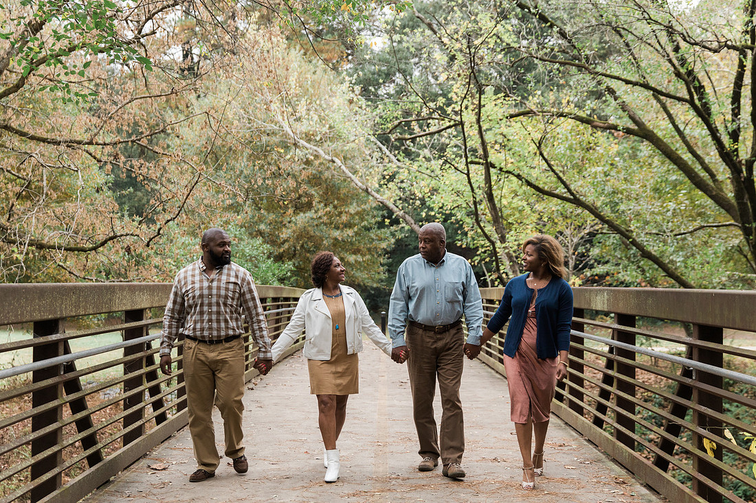 Parents and grown adult children smiling together outdoors during a family portrait session.