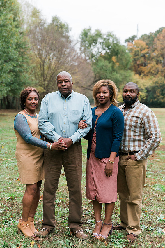 Parents and grown adult children smiling together outdoors during a family portrait session.