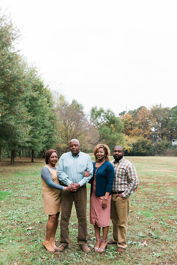 Parents and grown adult children smiling together outdoors during a family portrait session.