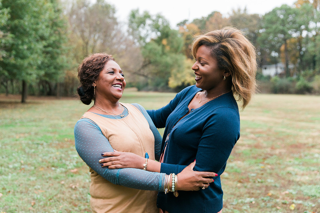 Parents and grown adult children smiling together outdoors during a family portrait session.