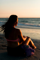 a high school senior girl looking out over the water next to her childhood stuffed animal, during sunset during her beach photo shoot.