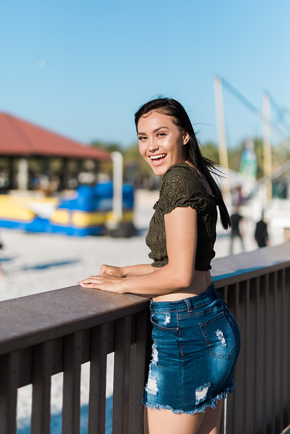 A High School Senior Girl laughing on a sunlit pier beachside.