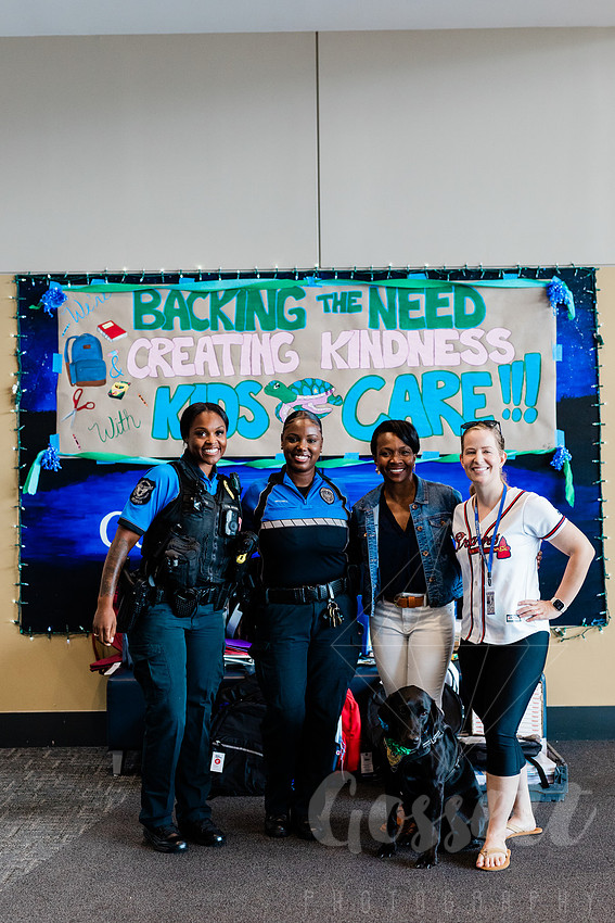 Cobb County Chairwoman Lisa Cupid and Cobb Police Officers stand together smiling at school supply drive, with colorful sign behind them. 